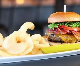 A burger with cheese and bacon, curly fries, and dill pickle.