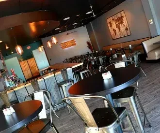Modern restaurant interior with bar, tables, booths, and a neon sign.