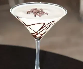 Frothy white drink in chocolate-drizzled martini glass, garnished with flakes.