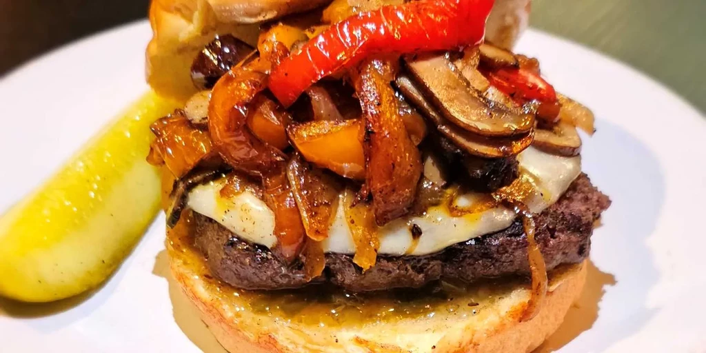 Gourmet burger with beef, cheese, caramelized onions, mushrooms, and gherkin.