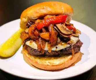 Gourmet burger with cheese, caramelized onions, mushrooms, peppers, and pickle spear.