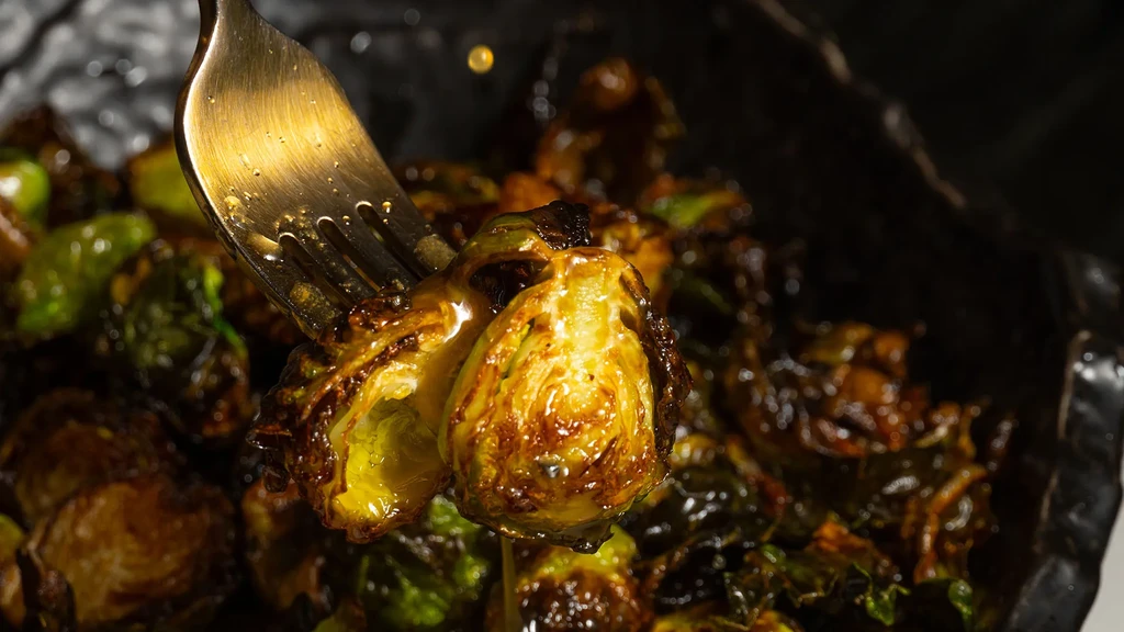 Close-up of a glossy, caramelized roasted Brussels sprout lifted by a fork.