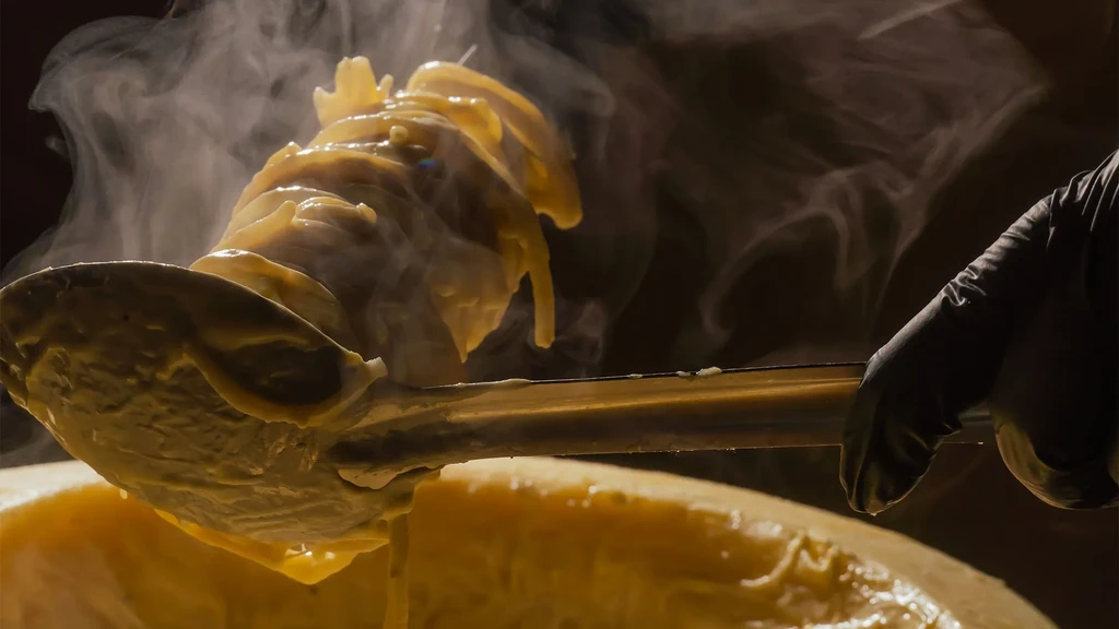 Steaming pasta with creamy sauce served from a large cheese wheel.