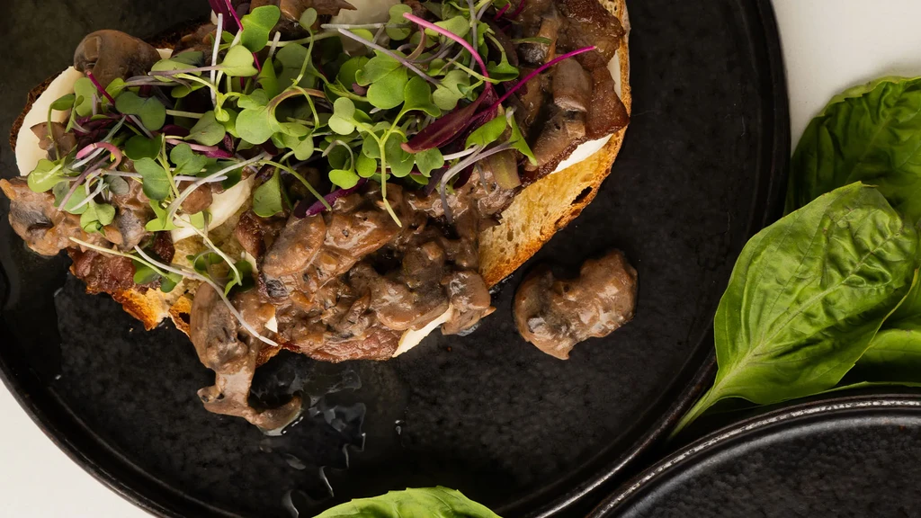 Creamy mushroom bruschetta topped with microgreens on a dark plate.