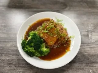 Plate of protein with dark sauce, broccoli, and green onions.
