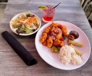 Orange chicken meal with rice, spring rolls, salad, and a cocktail.