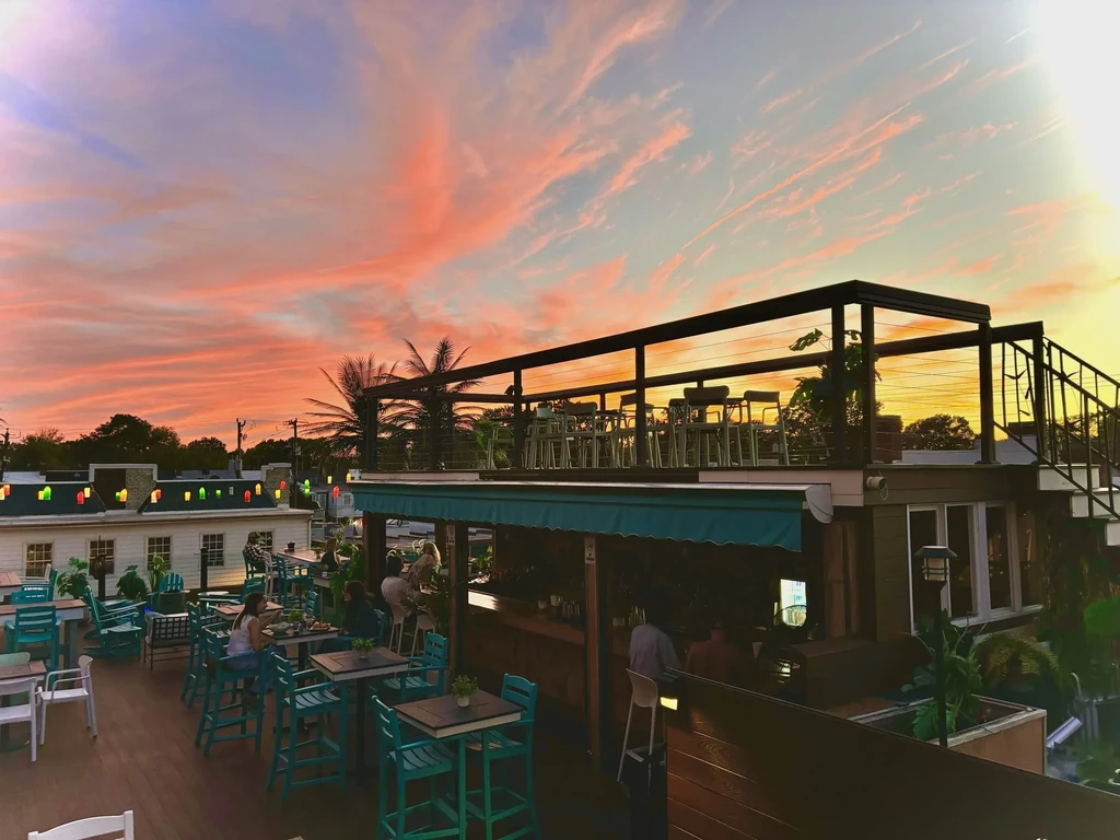 Multi-level rooftop restaurant with teal seating and patrons at sunset.