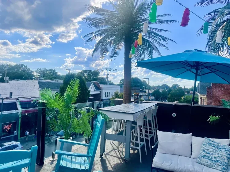 Sunny rooftop patio with tropical decor, colorful lanterns, and outdoor seating.