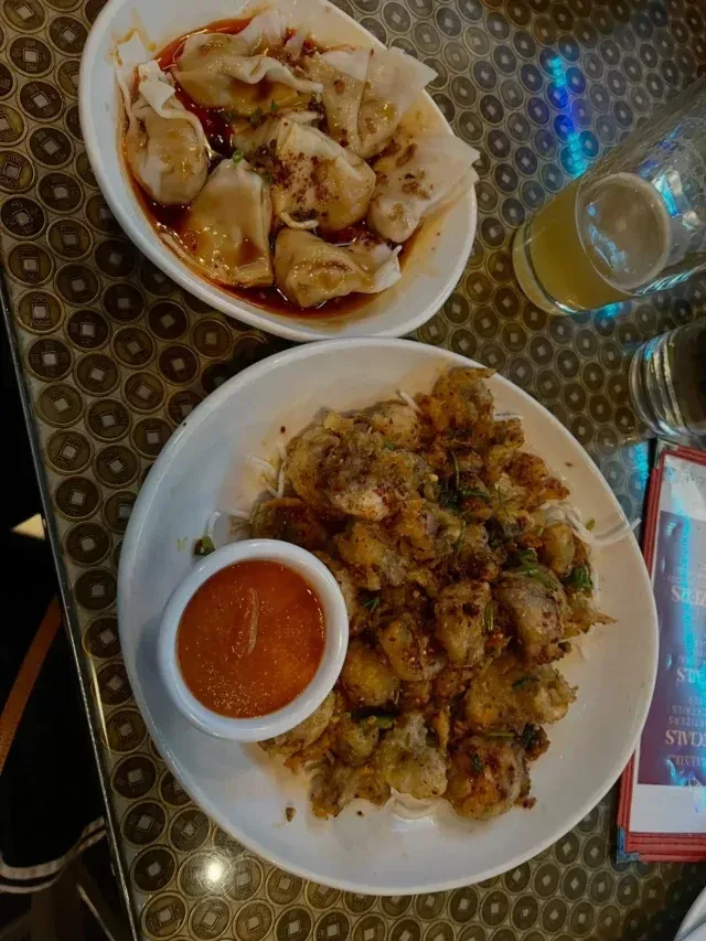 Overhead: dumplings, fried food, beer, and menu on coin-patterned table.