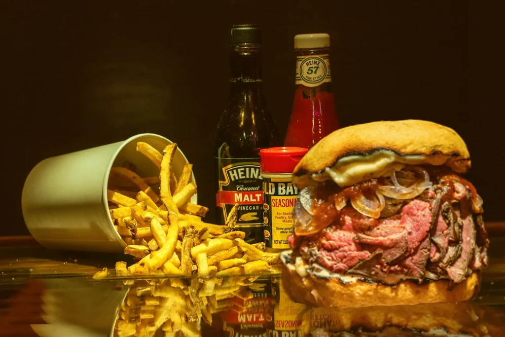 A close-up of a roast beef sandwich, spilling fries, and condiments.