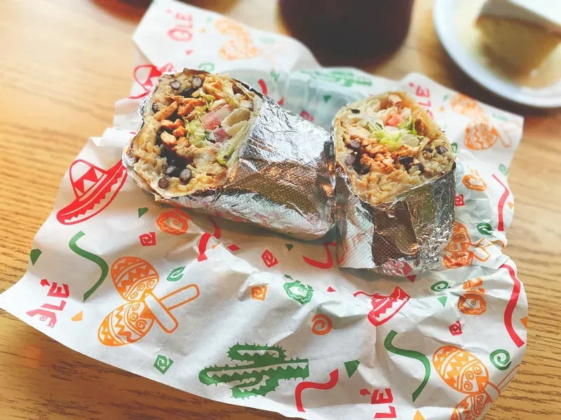 Cut burrito showing rice, beans, protein on festive paper.