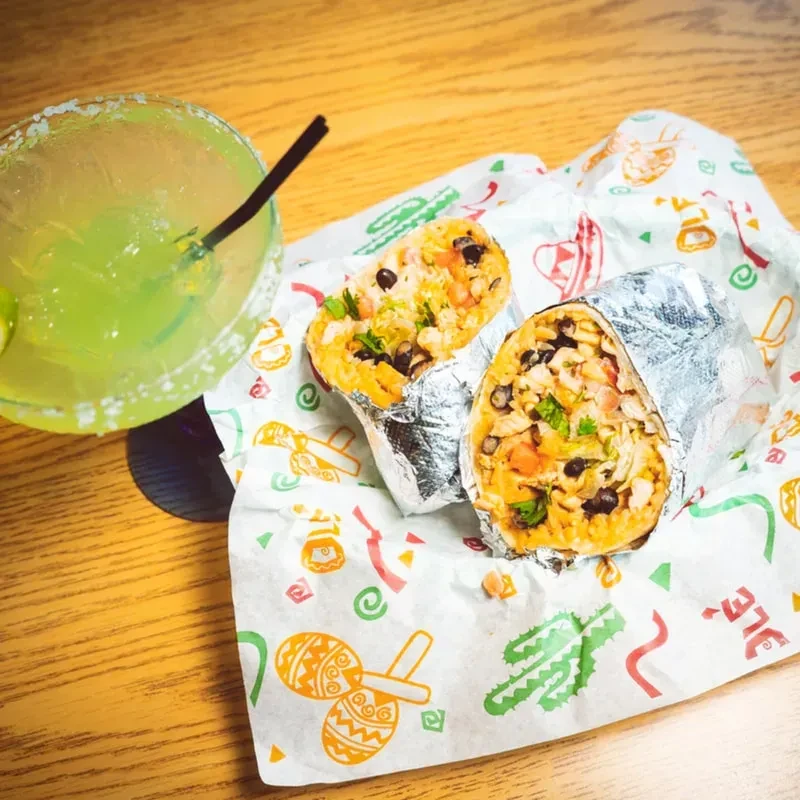 Two cut burritos and a margarita on Mexican-themed paper.