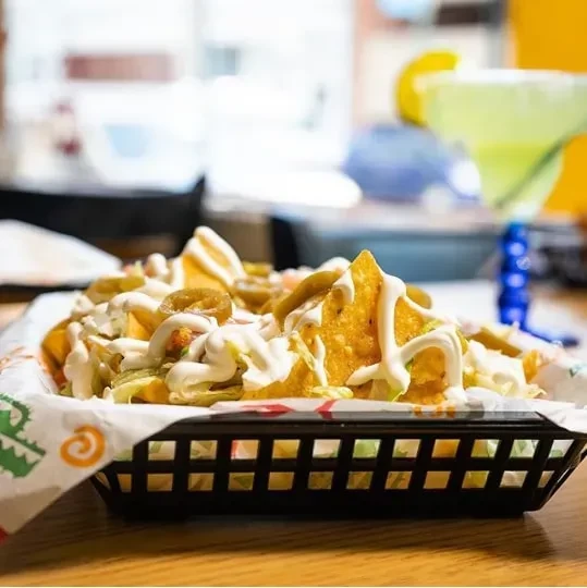 A basket of nachos with creamy sauce, jalapeños, and shredded lettuce.