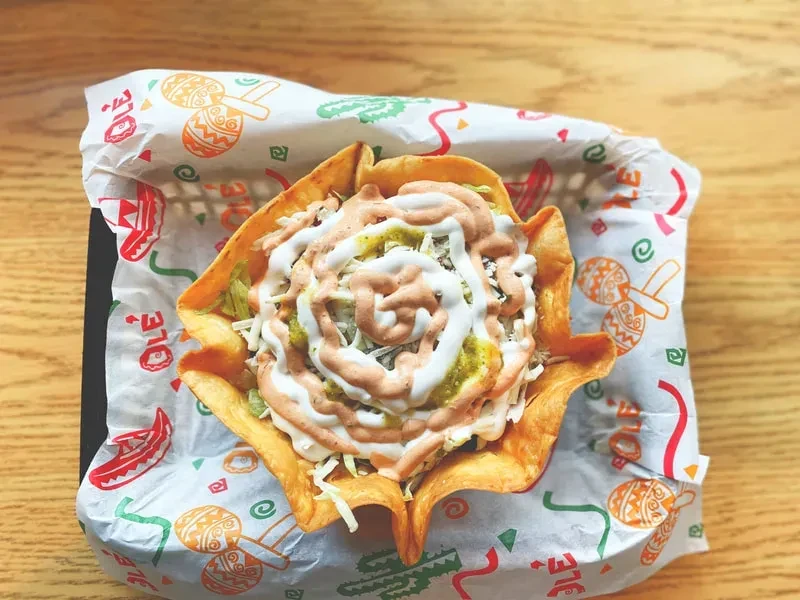 Crispy tortilla bowl taco salad with lettuce, cheese, and three sauces.