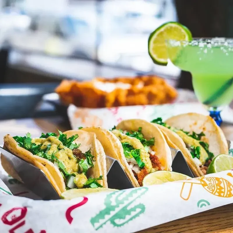 Several tacos with cilantro and onions next to a green margarita.