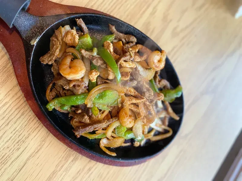 Sizzling cast-iron skillet with meat, shrimp, peppers, and onions.