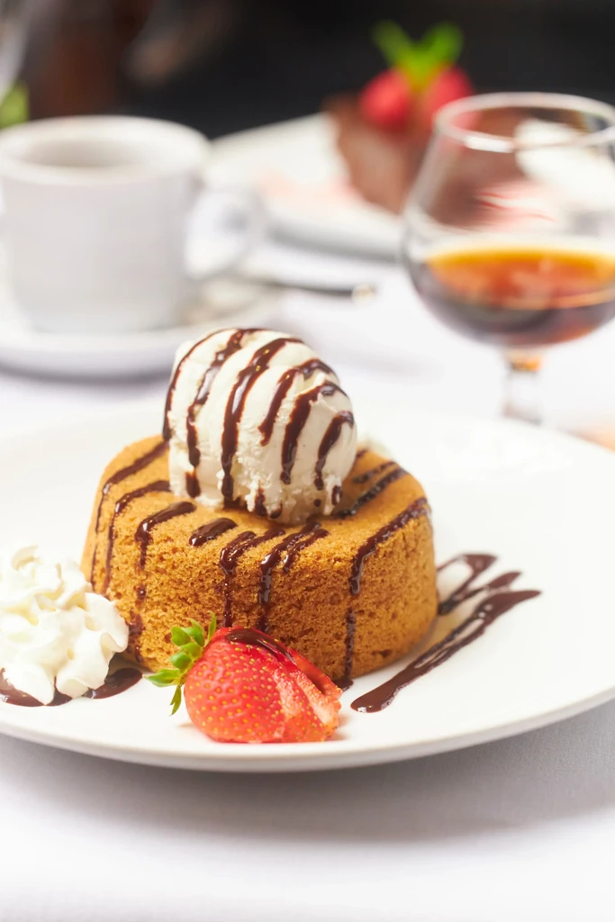 Golden-brown cake with vanilla ice cream, chocolate syrup, strawberry, whipped cream.
