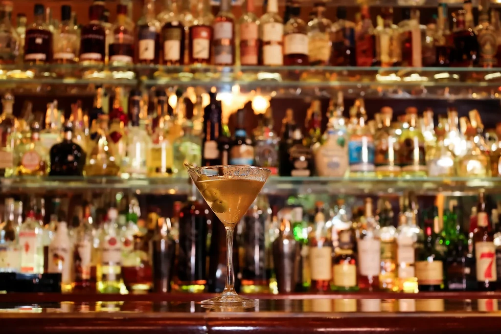 Close-up of an amber martini with olives at a blurred bar.