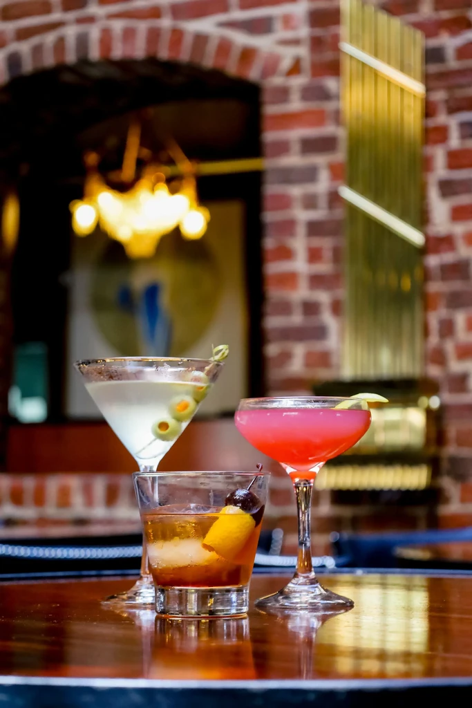 Martini, Old Fashioned, and pink cocktail on a polished wooden table.