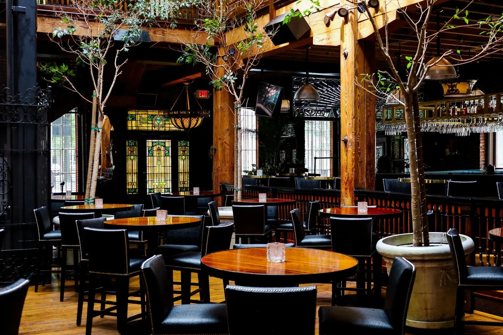 Upscale restaurant interior with wooden tables, bar, and stained-glass windows.