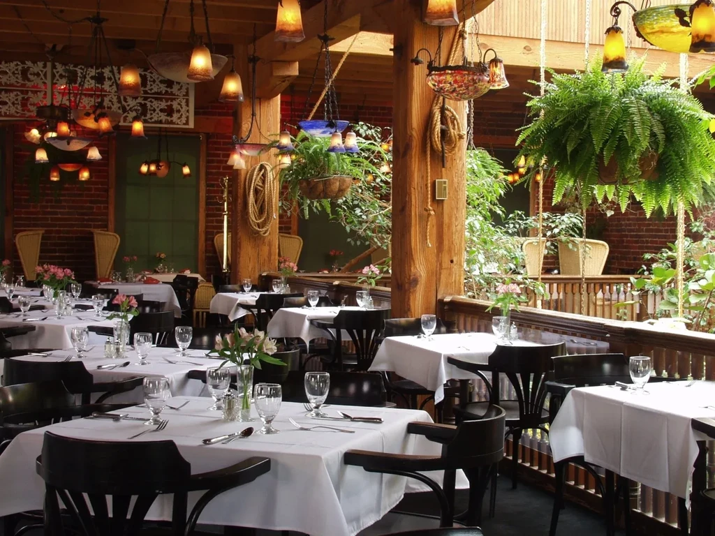 Empty restaurant dining room with set tables, wood beams, and warm lights.