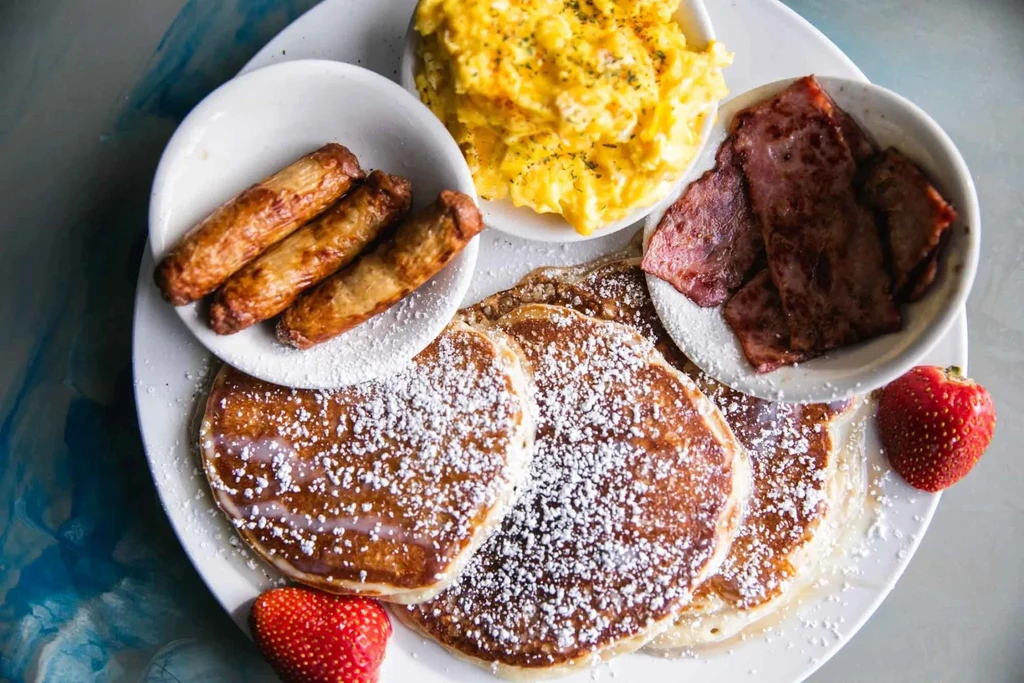 Breakfast plate: powdered pancakes, scrambled eggs, bacon, sausage, strawberries.