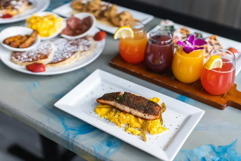 Salmon, pancakes, eggs, and colorful drinks on a swirling patterned table.