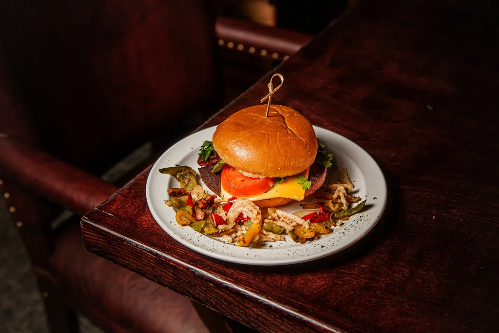 Gourmet burger with melted cheese, tomato, lettuce, and colorful vegetables.