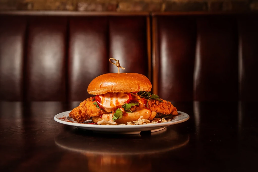 Fried chicken sandwich with tomato, cilantro, and sauce on a brioche bun.