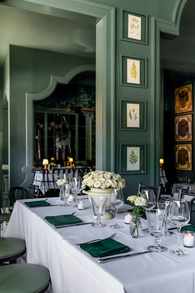 Elegant green restaurant interior with formal table settings and white rose centerpieces.