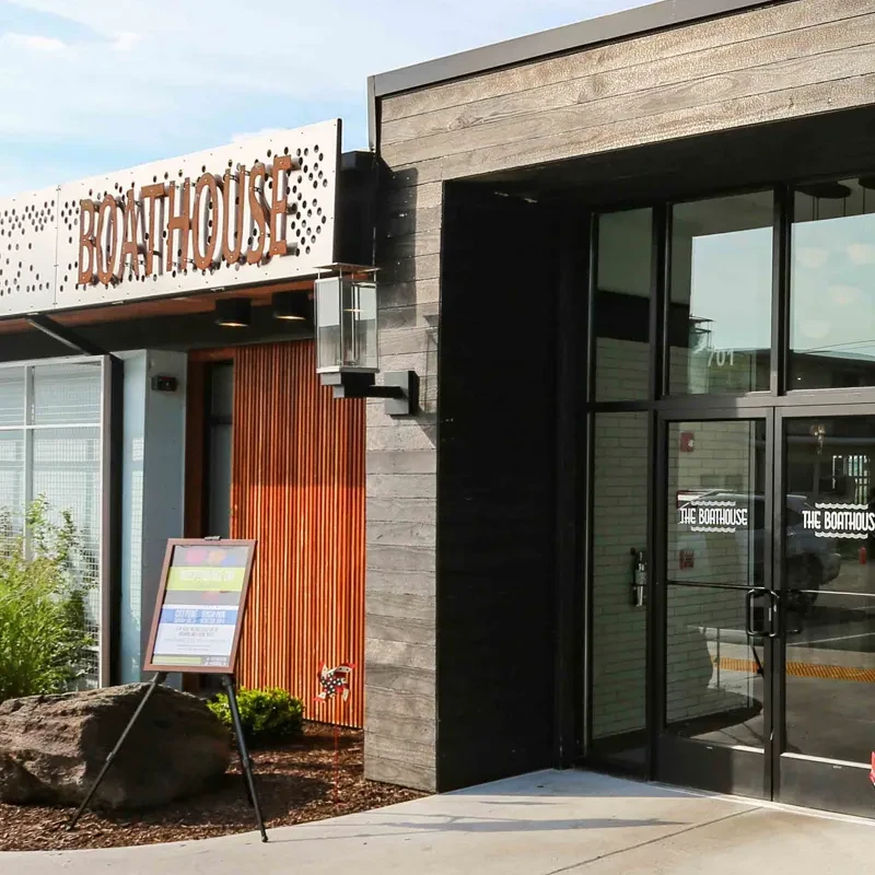 Modern "The Boathouse" restaurant exterior, dark wood paneling, glass doors.