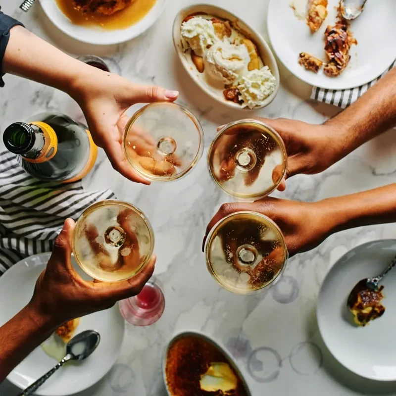 Overhead: Four hands toast champagne flutes among various dessert plates.