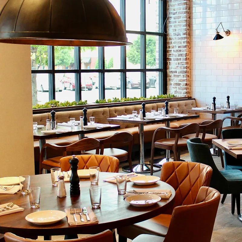 Empty modern restaurant dining room with set tables and window views.