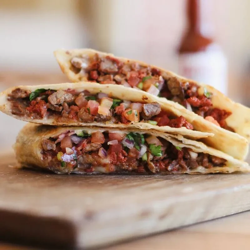 Stacked golden quesadilla halves with meat, pico de gallo, and melted cheese.