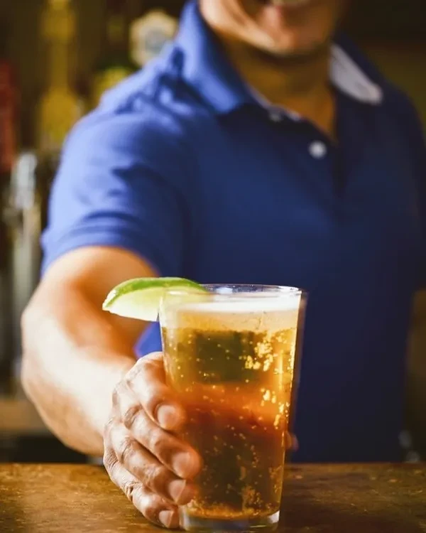 Hand holds a bubbly drink with lime on a wooden bar counter.