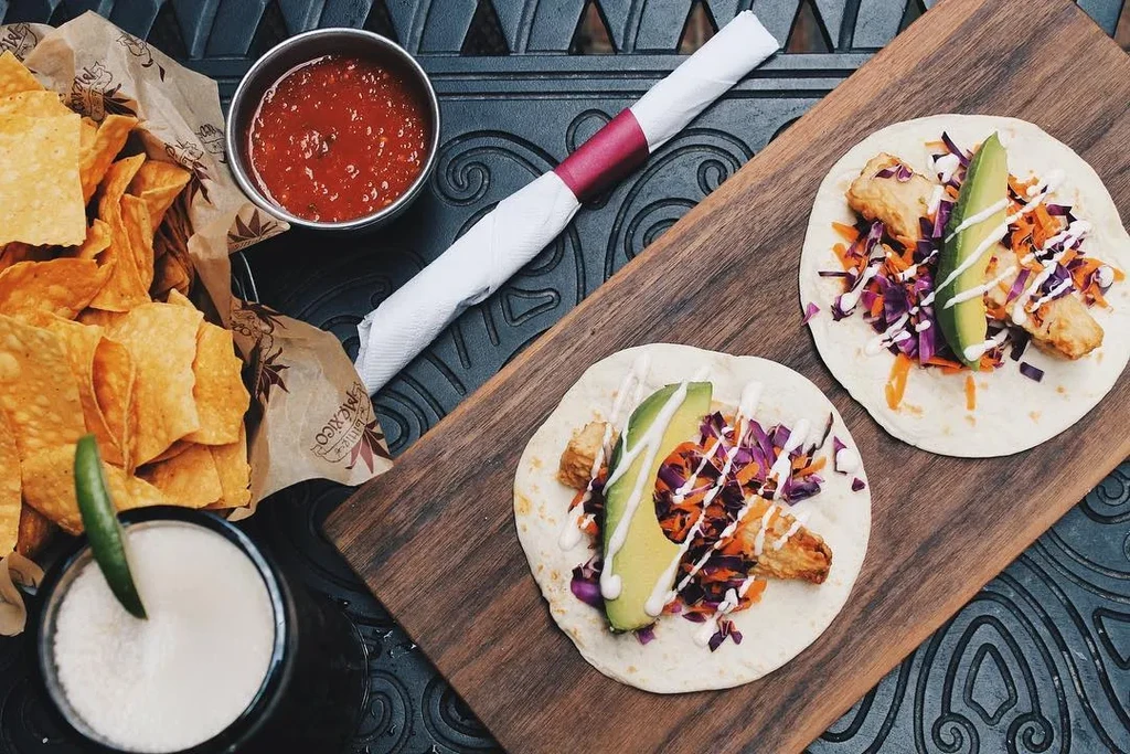 Overhead shot of Mexican fish tacos, chips, salsa, and drink.