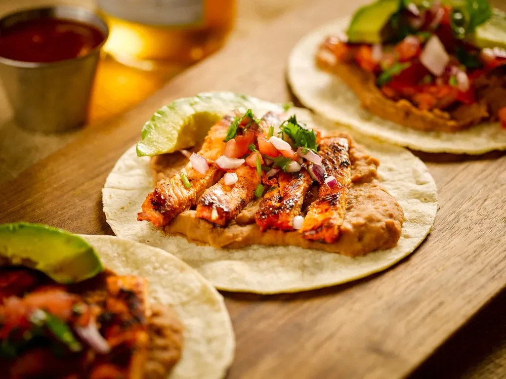 Three tacos with grilled meat, beans, pico de gallo, avocado.