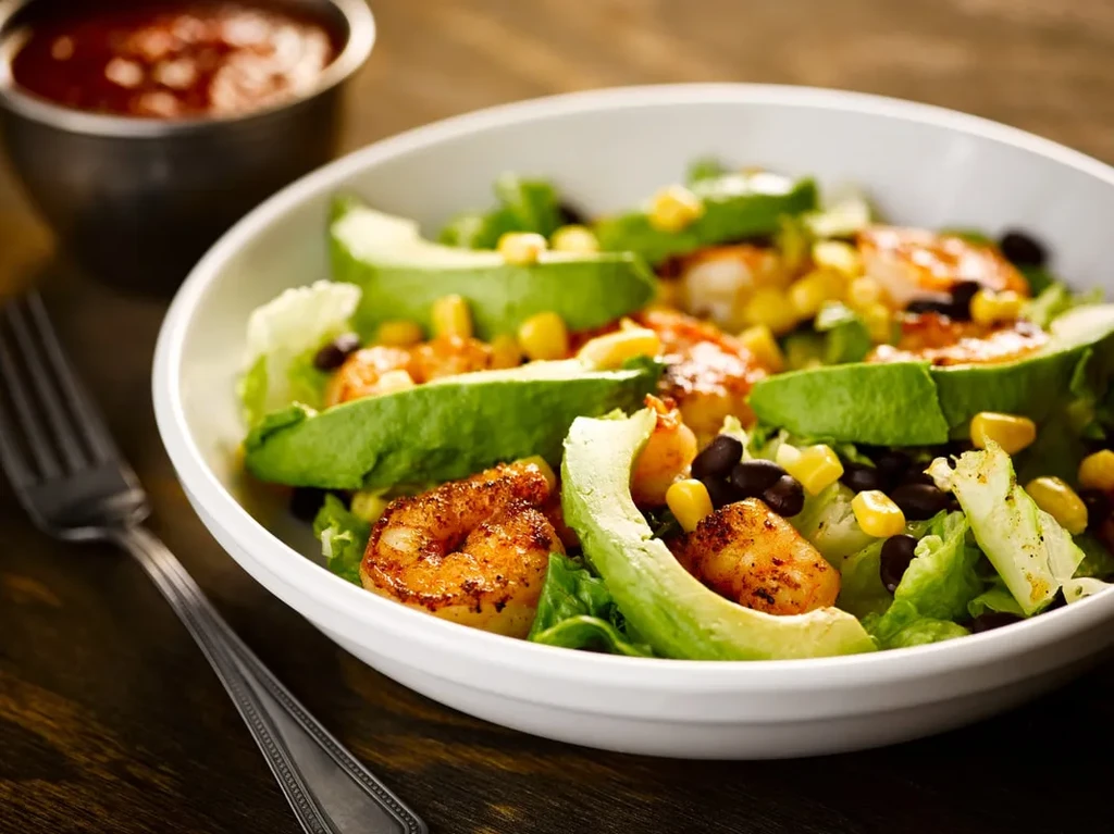 Shrimp salad with avocado, corn, and black beans in a white bowl.