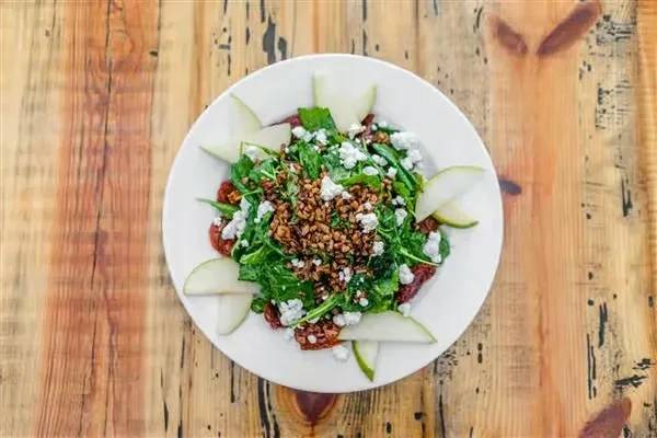 Flat lay salad with greens, cheese, nuts, and fruit on wood.