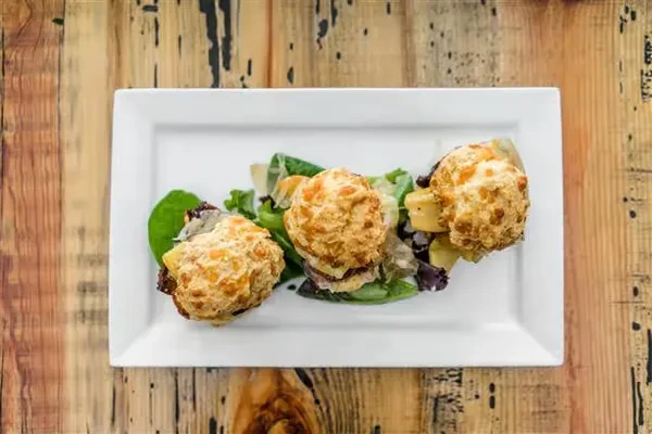 White plate with three golden-brown savory muffins, lettuce, and yellow dice.