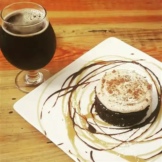 Frosted chocolate cake, sauced plate, and dark beer on wood.
