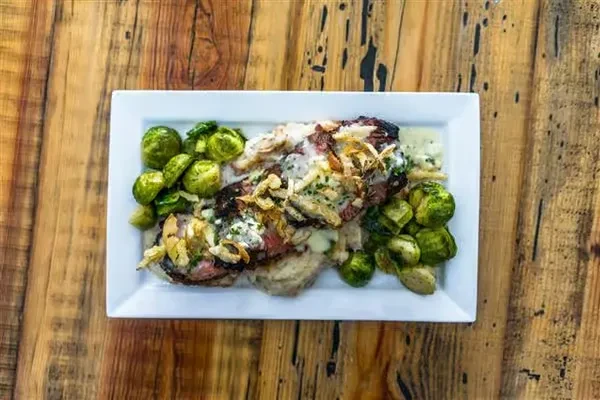 Plated meat with creamy sauce, herbs, and Brussels sprouts on rustic wood.