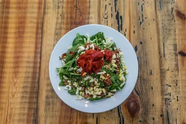 Fresh green salad topped with white crumbles and red peppers on wood.
