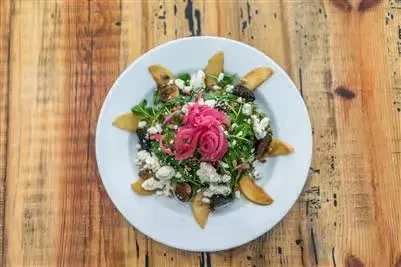 Green salad with white cheese, dark fruit, and pink onion rosette.