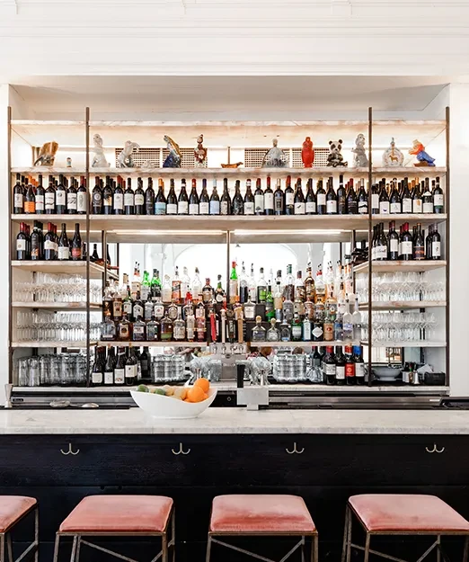 Well-lit, upscale bar with diverse drinks, marble counter, and pink stools.