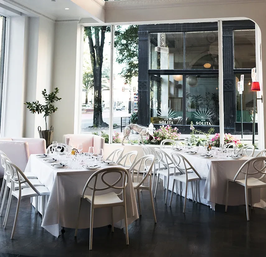Bright, elegant restaurant interior with set tables, pink booths, city view.