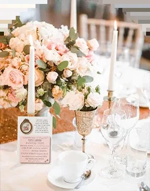 Elegant table setting: pink rose centerpiece, lit candles, gold runner, text card.