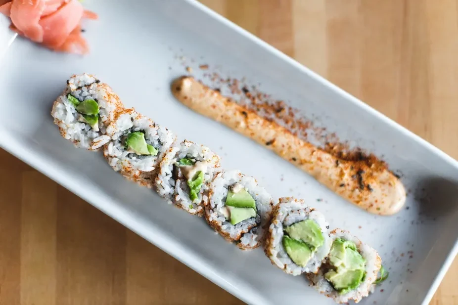 Overhead sushi roll, avocado, spicy flakes, orange sauce, and pink ginger.