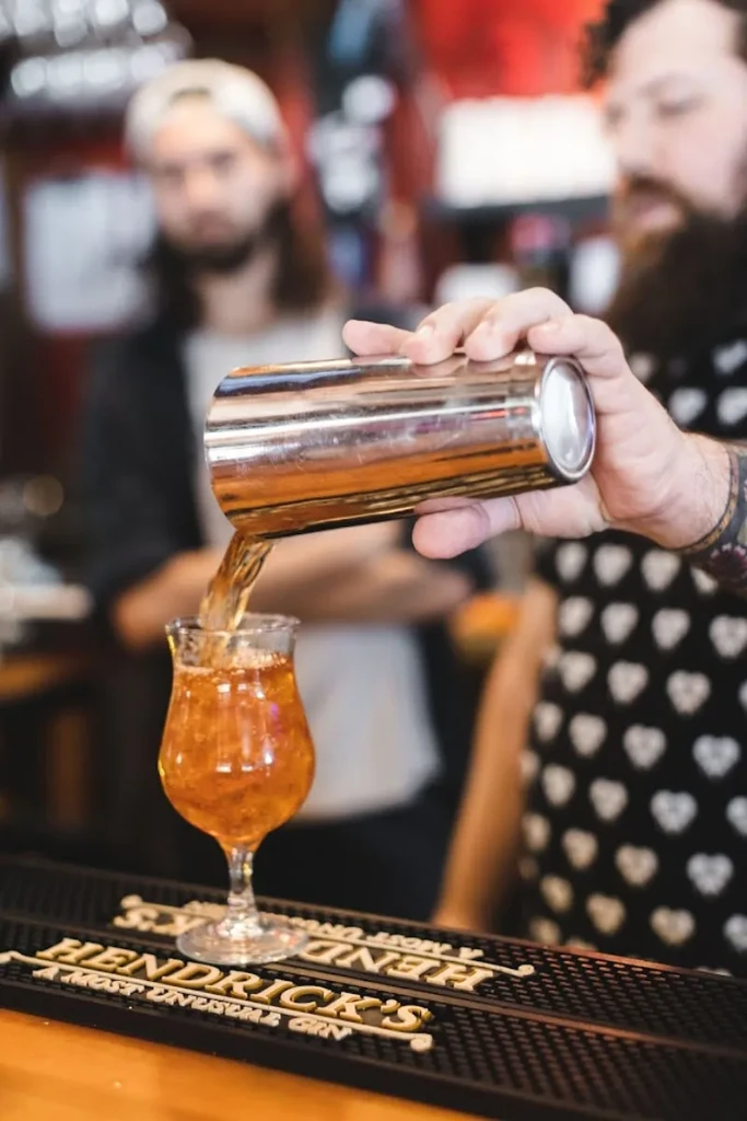 Bartender's hands pour amber drink into stemmed glass on Hendrick's mat.