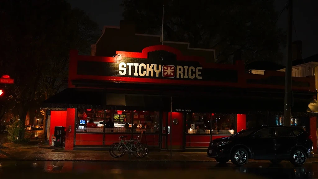 Red and black Sticky Rice restaurant exterior at night, wet street.